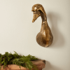 Bronze duck wall sculpture wearing aviator goggles above a rustic wood mantel with greenery, adding playful charm to a space designed by Urban Goods & Garden in Wilmington, NC.