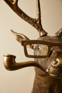 Close-up of a bronze deer sculpture wearing glasses and holding a pipe, showcasing the detailed and whimsical decor available at Urban Goods & Garden in Wilmington, NC.